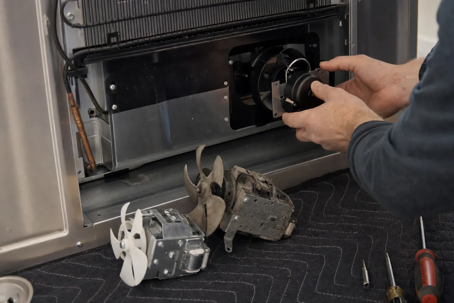 Replacement fan motor being fitted into the lower bay of a built-in unit, the removed motor and its blade on the floor alongside